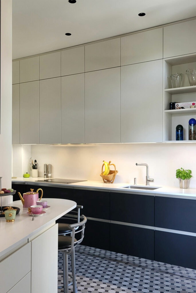 Une cuisine bicolore beige et noire. Ambiance graphique. Au sol, une mosaïque en grès cérame teinté dans la masse ancre visuellement l'espace. Les meubles toute hauteur optimisent les rangements jusqu'au plafond, tandis que le plan de travail et la crédence en quartz ajoutent une touche de finesse et de durabilité.