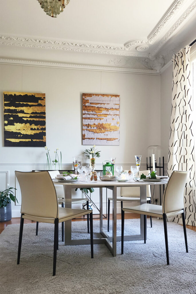 Salle à manger avec des moulures anciennes. Table ronde et 4 chaises en cuir beige. Rideaux en lin graphiques. Lampadaire métal noir et verre transparent. Console en métal noir.
