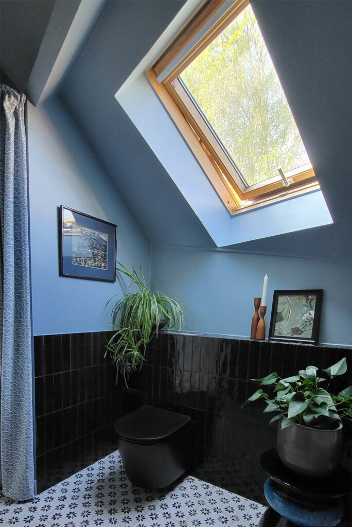 Salle de bain sous combles. Carrelage zellige noir en soubassement. Murs peints en bleu nuit. WC de couleur noir se fond avec le carrelage noir du soubassement.