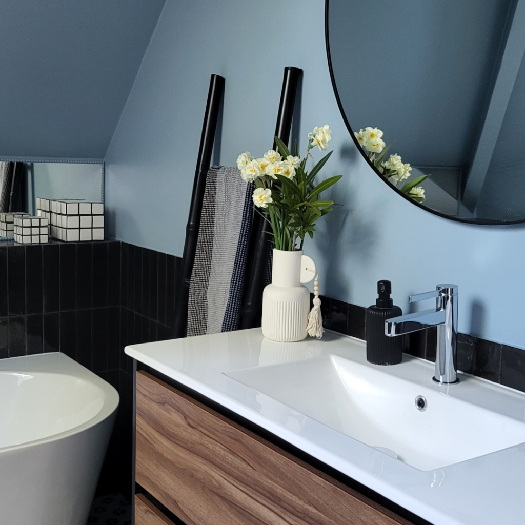 Meuble de salle de bain suspendu en bois avec vasque blanche devant un mur bleu mat et miroir rond.