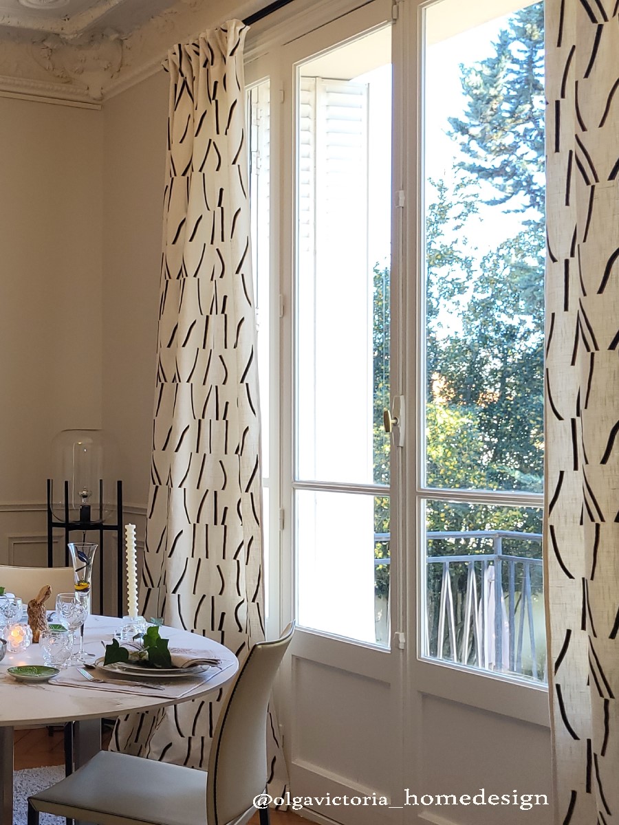 Salle à manger lumineuse avec rideaux sol-plafond à motif graphique noir et blanc, table ronde dressée, moulures au plafond, style haussmannien Vincennes.
