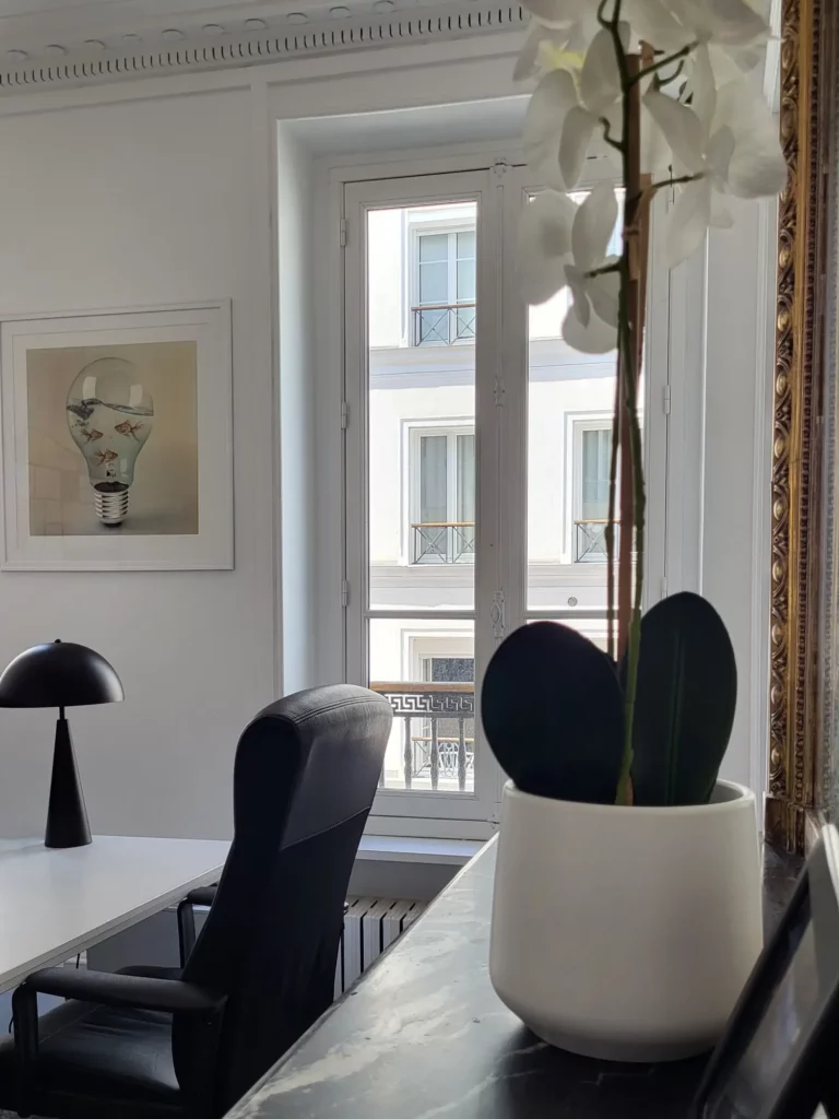 Bureau de direction avec cheminée en marbre noir, miroir doré, lampe en métal noire, fauteuil cuir noir et orchidée blanche.