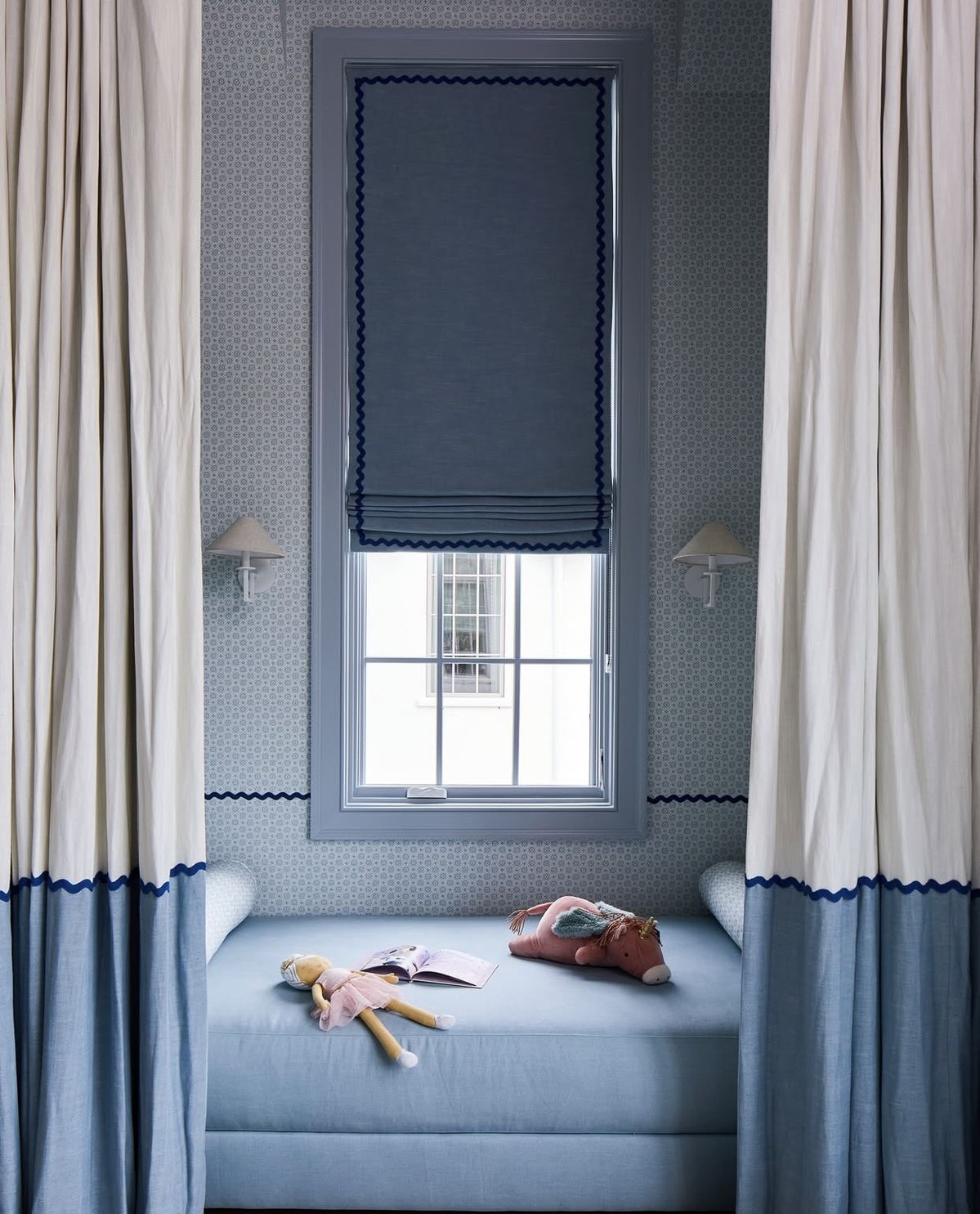 Rideaux sol-plafond blanc et bleu avec ruban décoratif bleu marine, store bateau bleu assorti, chambre enfant avec un lit dans un alcove et papier peint géométrique bleu.
