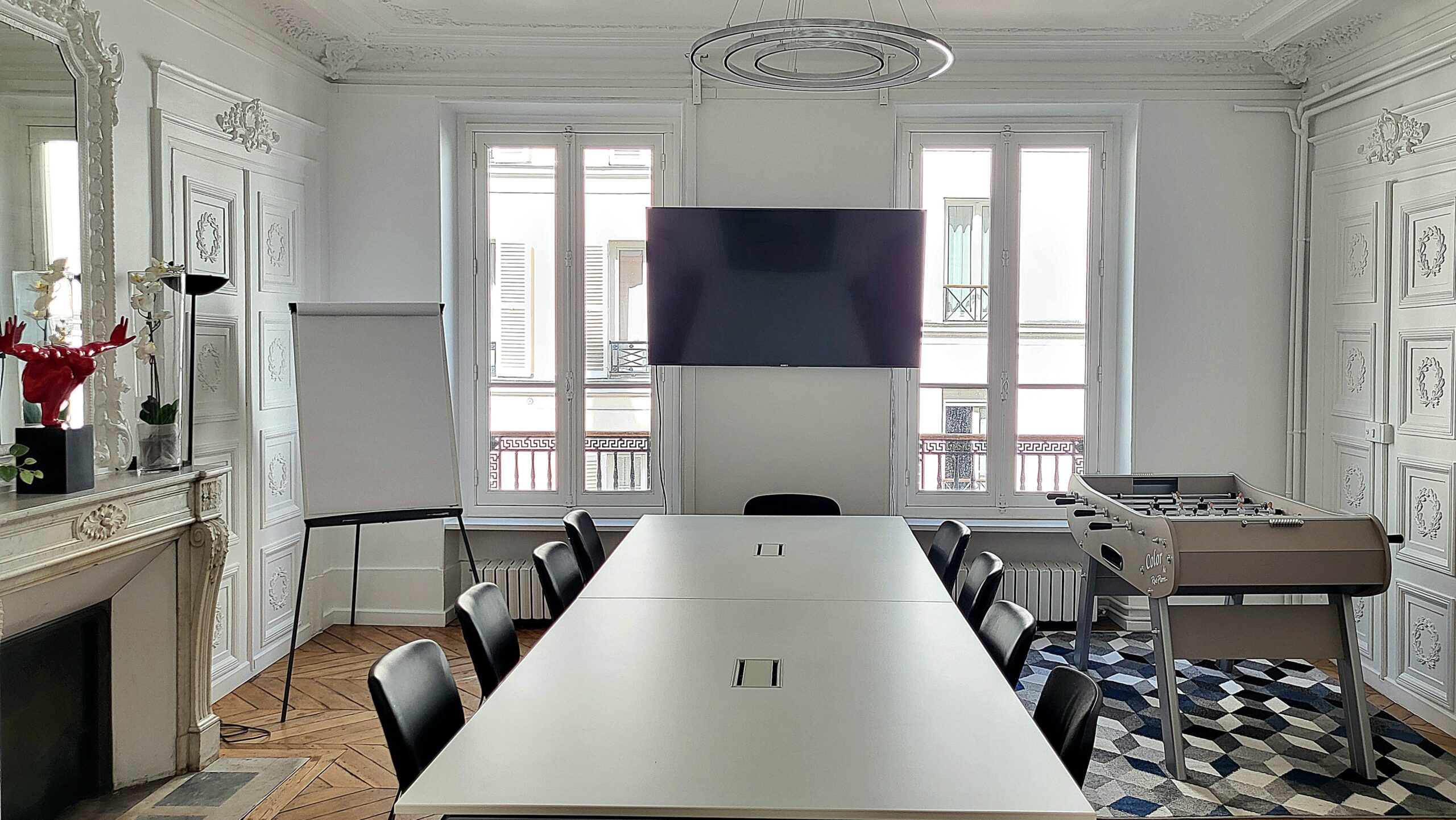 salle de reunion avec une grande table blanche, chaises noires, coin détente avec baby-foot.
