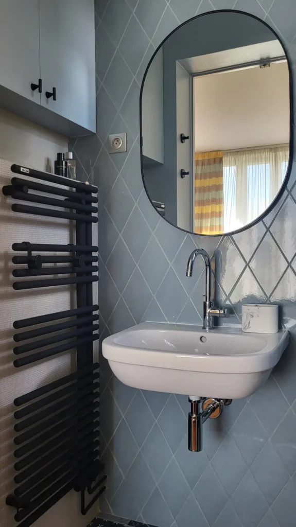Salle de bain avec miroir ovale, sèche-serviettes noir et carrelage bleu — maison ancienne Vincennes